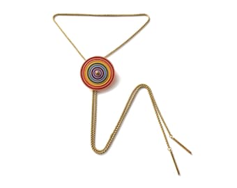 May include: A gold chain bolo tie with a colorful circular pendant. The pendant has concentric circles of red, orange, yellow, green, blue, indigo, and violet.