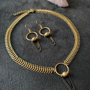 May include: A gold necklace with a chain link design and a pendant with a circle and a small ball. Matching earrings with a circle and a small ball dangle from gold hooks.