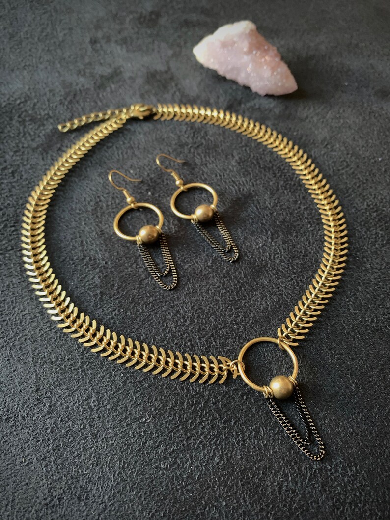 May include: A gold necklace with a chain link design and a pendant with a circle and a small ball. Matching earrings with a circle and a small ball dangle from gold hooks.