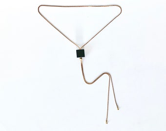 May include: A gold chain necklace with a black square pendant and two long brown cords.
