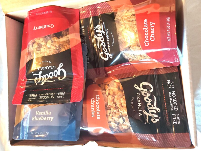 K&ouml;nnte beinhalten: Eine Schachtel gef&uuml;llt mit Goody's Granola-Beuteln. Die Geschmacksrichtungen sind Cranberry, Chocolate Cherry, Vanilla Blueberry und Chocolate Chunks. Jeder Beutel wiegt 112g und ist milchfrei, ohne Zusatz von Konservierungsstoffen und glutenfrei.