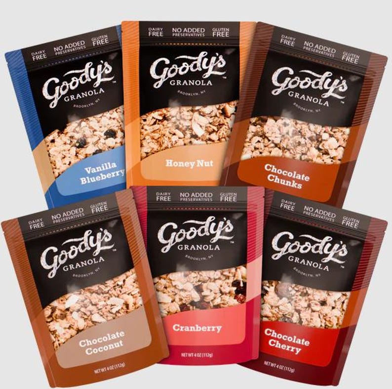 K&ouml;nnte beinhalten: Sechs Beutel Goody's Granola in verschiedenen Geschmacksrichtungen: Vanille Blaubeere, Honig Nuss, Schokoladenst&uuml;cke, Schokoladen Kokosnuss, Cranberry und Schokoladen Kirsche. Jeder Beutel hat eine schwarze Oberseite mit dem Markennamen und der Geschmacksrichtung.