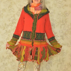 May include: A red, green and yellow patchwork jacket with a ruffled hem and a green hooded collar. The jacket is worn over a pair of patterned leggings and black ankle boots.
