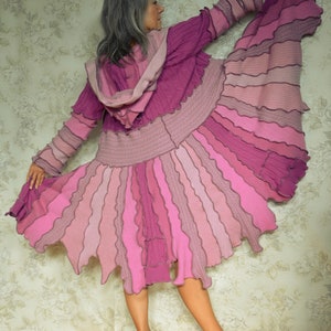 May include: A long, pink, layered cardigan with a hood. The cardigan is made of a soft, knitted fabric and has a flowing, asymmetrical hemline.