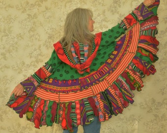 May include: A green, red, and purple knitted cardigan with a colorful fringe hem. The cardigan is worn over blue jeans.
