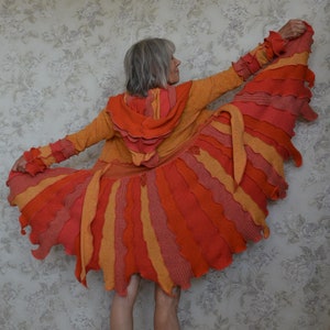 May include: A long, red, orange and yellow striped hooded cardigan with a ruffled hem. The cardigan is made of a soft, knitted fabric and has a relaxed fit.