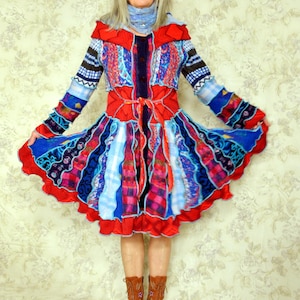 May include: A vibrant, patchwork dress in red, blue, and patterned fabrics. The dress features long sleeves, a cinched waist, and a flared skirt. The model is wearing brown boots. The dress is a unique, artistic garment.