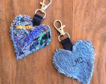 May include: Two denim heart-shaped keychains. One keychain is made of patchwork denim with colorful fabric accents. The other keychain is solid denim with the initials "LMD" embroidered in black thread.