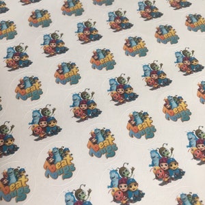 May include: A sheet of white paper with multiple round stickers featuring the characters from the show "Beat Bugs". The stickers have a white border and a blue background with the text "Beat Bugs" in white letters. The characters are a group of colorful insects with smiling faces.