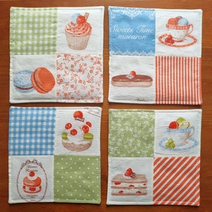 May include: Set of four square fabric coasters with different patterns. Each coaster features a different dessert or pastry illustration, including a cupcake, macarons, a pastry, and a cake. The coasters are ideal for protecting surfaces from heat and spills.