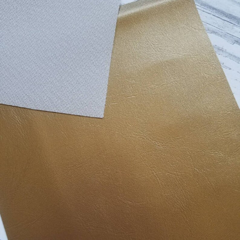 Puede incluir: Dos piezas de tela, una blanca y una dorada. La tela dorada tiene una textura similar al cuero.