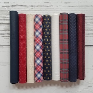 May include: Eight rolls of patterned faux leather in various colors and designs, including red, white, blue, and gold. The rolls are arranged horizontally on a white wooden surface.