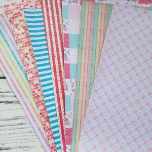 May include: Assortment of patterned craft paper in pink, blue, and white with glitter accents. The paper has various patterns including stripes, polka dots, and plaid.