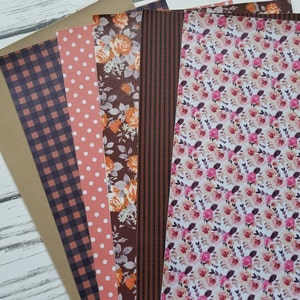 May include: A set of six patterned craft paper sheets in various fall colors. The sheets feature a brown gingham pattern, white polka dots on a peach background, a floral pattern with orange roses, brown stripes, and a floral pattern with pink roses on a white background.