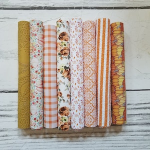May include: Eight rolls of patterned fabric in various fall colors, including orange, yellow, and white. The patterns include paisley, floral, plaid, and pumpkin designs.