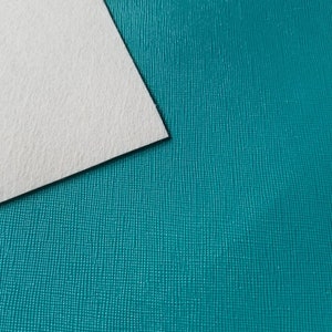 May include: A close-up of a teal textured surface with a white piece of paper on top of it.
