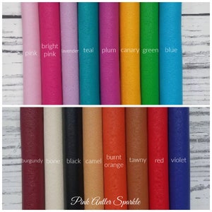 May include: A collection of 18 leather swatches in various colors, including pink, teal, plum, canary, green, blue, burgundy, bone, black, camel, burnt orange, tawny, red, and violet. The swatches are arranged in two rows, with the top row showing brighter colors and the bottom row showing darker colors. The text "Pink Antler Sparkle" is printed at the bottom of the image.