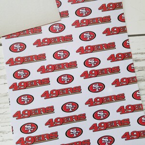 Puede incluir: Tela blanca con un patr&oacute;n repetido de logotipos rojos y dorados de los San Francisco 49ers.