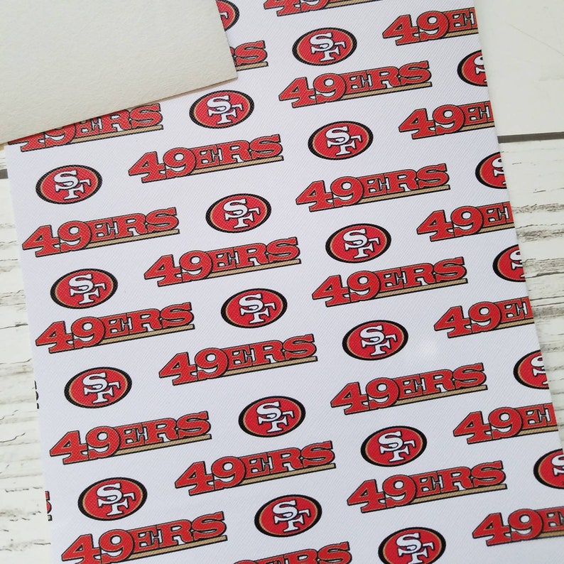 Puede incluir: Tela blanca con un patr&oacute;n repetido de logotipos rojos y dorados de los San Francisco 49ers.