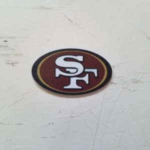 Puede incluir: Un logotipo de los San Francisco 49ers en rojo, blanco y dorado sobre un fondo blanco.