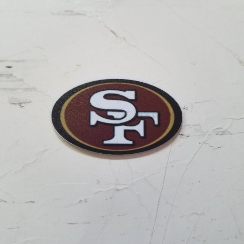 Puede incluir: Un logotipo de los San Francisco 49ers en rojo, blanco y dorado sobre un fondo blanco.