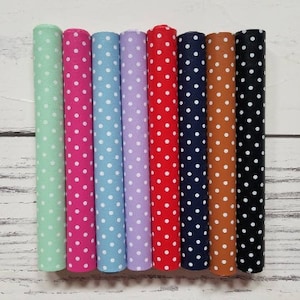 May include: Eight rolls of fabric with white polka dots on different colored backgrounds. The colors are mint green, pink, light blue, lavender, red, navy blue, brown, and black.