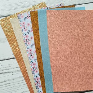 May include: A set of six different patterned craft sheets. The sheets include a gold glitter sheet, a beige sheet with a textured pattern, a floral patterned sheet, a cork sheet, a light blue glitter sheet, and a peach colored sheet with a textured leather look.