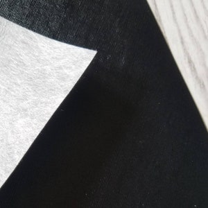 May include: A close-up of black fabric with a white, textured, triangular piece of fabric overlapping it.