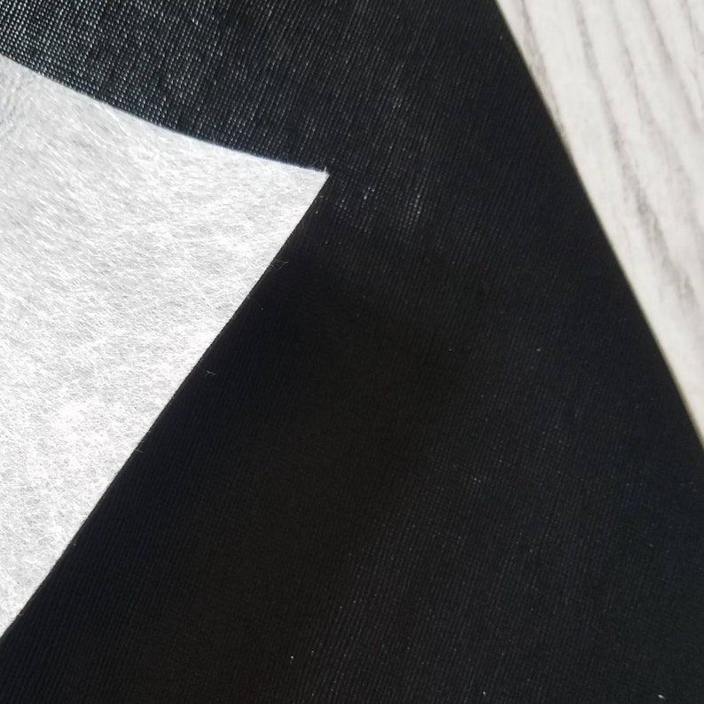 May include: A close-up of black fabric with a white, textured, triangular piece of fabric overlapping it.