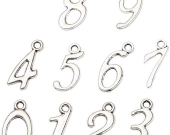 May include: Silver charm pendants in the shape of the numbers 0 through 9. Each charm has a loop at the top for attaching to a necklace or bracelet.