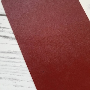 May include: A close-up of a deep red textured leather sheet. The leather has a subtle sheen and a fine grain pattern.
