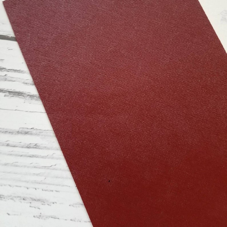 May include: A close-up of a deep red textured leather sheet. The leather has a subtle sheen and a fine grain pattern.