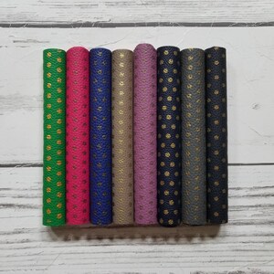 May include: Eight rolls of faux leather with a textured surface and gold polka dots. The rolls are in the following colors: green, pink, blue, beige, purple, navy blue, gray, and black.