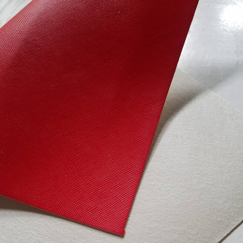 May include: A close-up of a red textured leather sheet with a white backing.