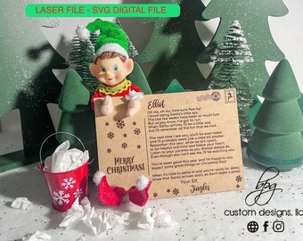 May include: A brown card with a Christmas message from an elf named Elliot. The card features a red and green elf with a white hat and a red bucket with snowflakes. The card reads "Merry Christmas!" and includes a message from the elf about being Santa's little spy.