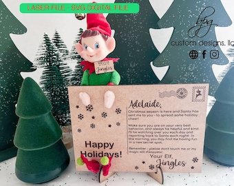 May include: A brown wooden postcard with a green elf holding a sign that says "Hello Jingles". The postcard has the text "Happy Holidays!" and "Adelaide, Christmas season is here and Santa has sent me to you - to spread some holiday cheer! Make sure you are on your very best behavior, and always be helpful and kind. I'll be watching over you each day and reporting back to Santa each night! In the morning, you may find me having fun in a new secret spot. Remember - please don't touch me or my magic will disappear. Your Elf, Jingles".