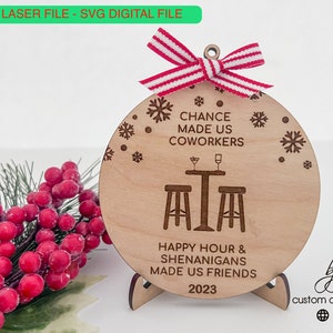 May include: A wooden Christmas ornament with a white background and brown text. The ornament reads "Chance made us coworkers, Happy Hour & Shenanigans made us friends, 2023". The ornament is decorated with snowflakes and a small illustration of a bar with two stools.