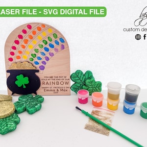 May include: A wooden rainbow craft kit with a pot of gold at the end. The kit includes paint, glitter, and a paintbrush. The text on the wood reads "You are the pot of gold at the end of our rainbow. Happy St. Patrick's Day Emma & Max 2023."
