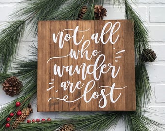 May include: A wooden sign with the text "Not all who wander are lost" in white lettering on a brown background.