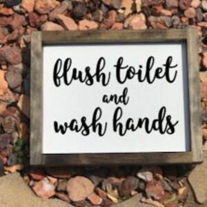 May include: White wooden sign with black text that reads "flush toilet and wash hands".