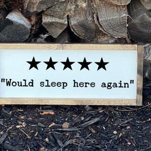 Op de afbeelding: Een wit houten bord met een bruin frame. Het bord heeft vijf zwarte sterren en de tekst "Would sleep here again".
