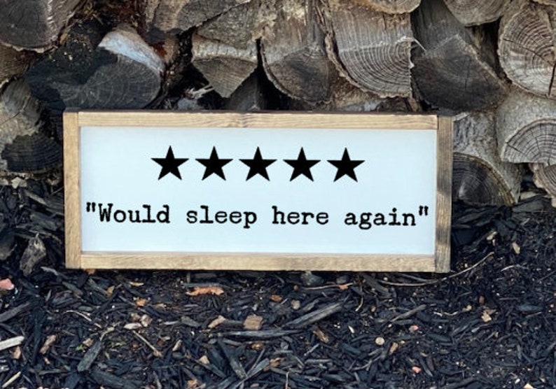 Op de afbeelding: Een wit houten bord met een bruin frame. Het bord heeft vijf zwarte sterren en de tekst "Would sleep here again".