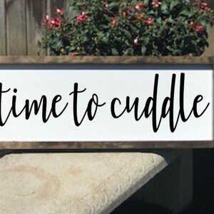May include: A white wooden sign with a brown frame, featuring the text "time to cuddle" in black cursive lettering.