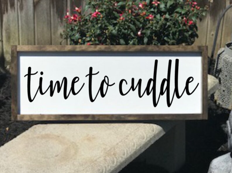 May include: A white wooden sign with a brown frame, featuring the text "time to cuddle" in black cursive lettering.
