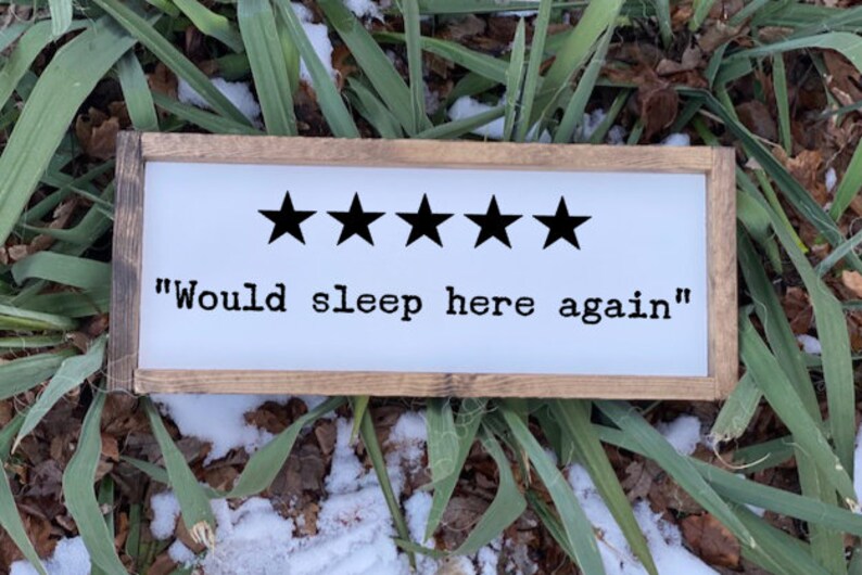 Op de afbeelding: Een wit houten bord met een bruin frame. Het bord heeft vijf zwarte sterren en de tekst "Would sleep here again".