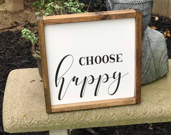 May include: A wooden framed sign with the text "CHOOSE happy" in black cursive lettering on a white background.