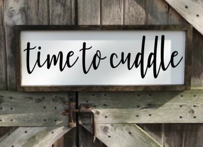 May include: A white wooden sign with black lettering that reads "time to cuddle". The sign is hanging on a wooden wall.