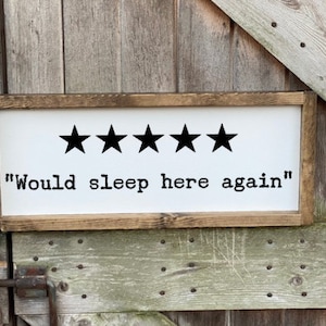 Op de afbeelding: Een wit houten bord met een bruin frame. Het bord heeft vijf zwarte sterren en de tekst "Would sleep here again".