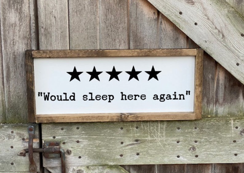 Op de afbeelding: Een wit houten bord met een bruin frame. Het bord heeft vijf zwarte sterren en de tekst "Would sleep here again".