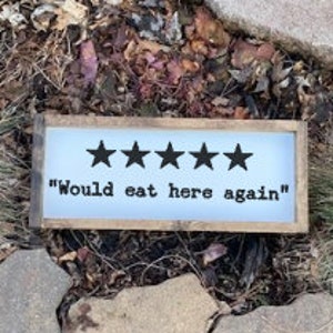 May include: A rustic wooden sign with a white background and black text. Five black stars are displayed above the text "Would eat here again".